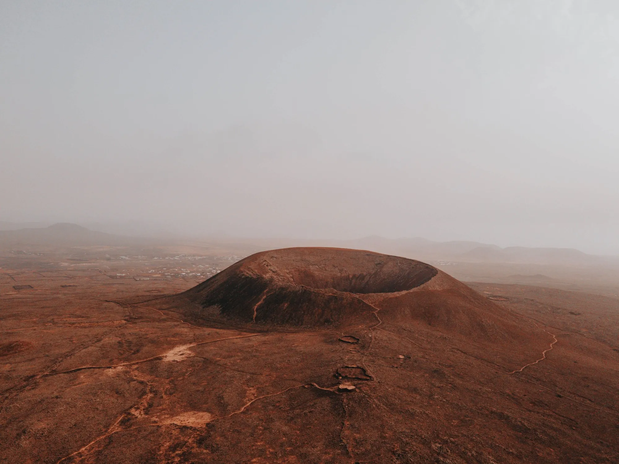 A round volcanic crater on a red-brown plain, with a path to the rim