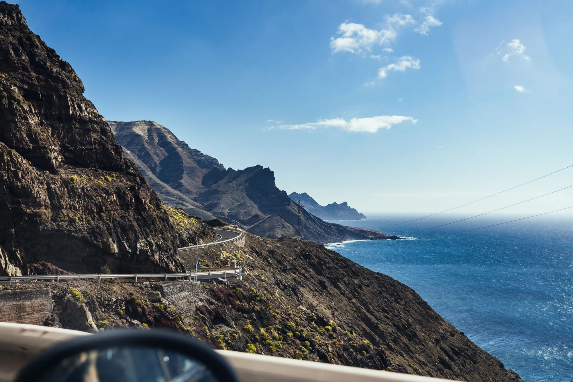 A winding coast road cut into steep dark cliffs above a deep blue sea on Gran Canaria