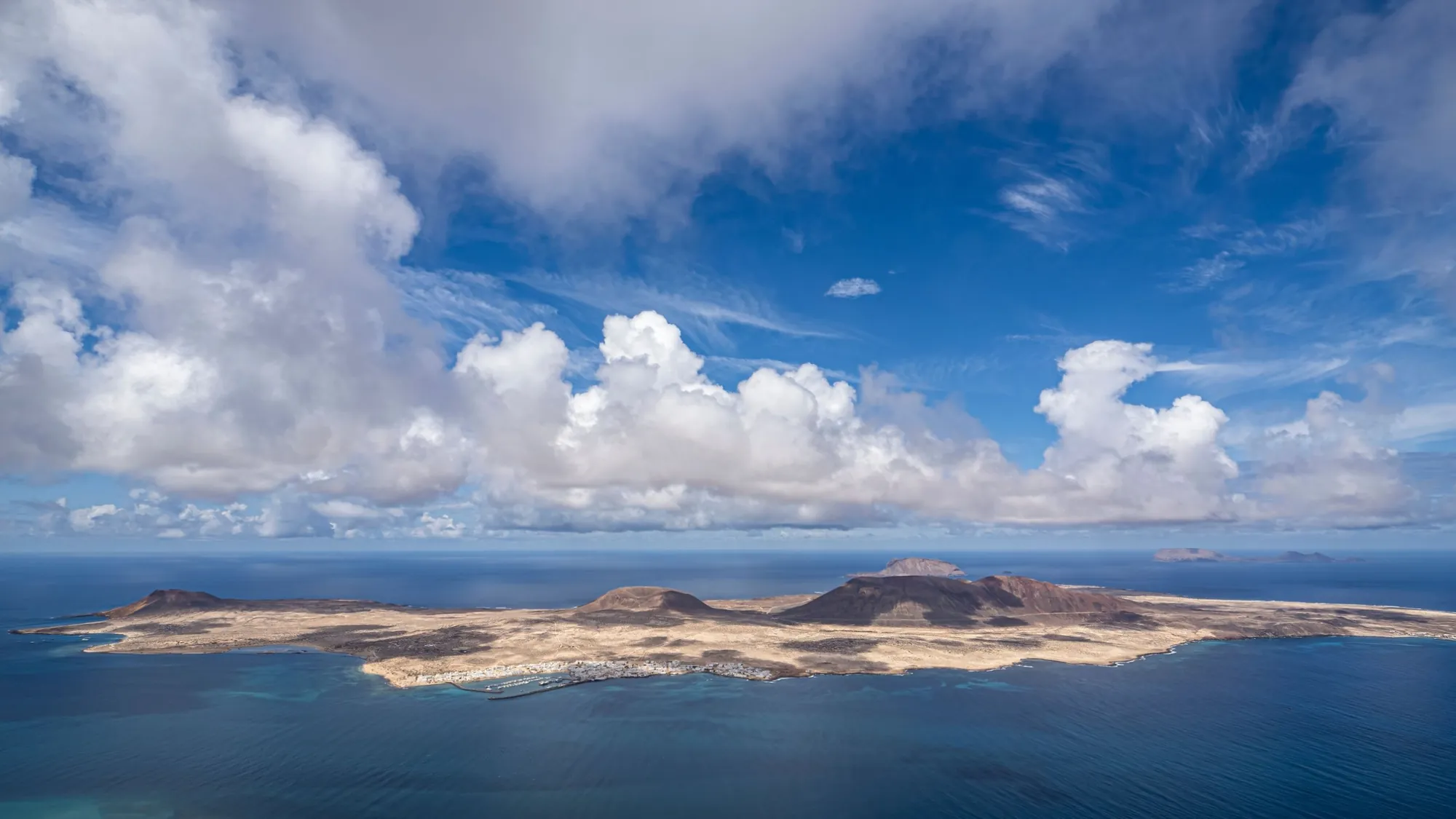 La Graciosa seen from the cliffs of Lanzarote, with its volcanoes and the harbour village under big clouds