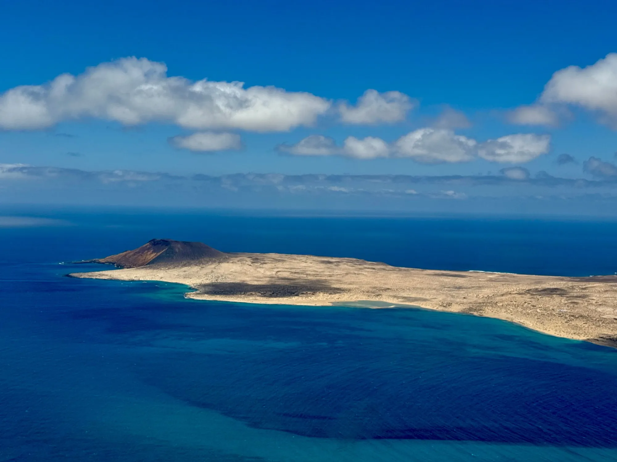 La Graciosa seen from above, with a volcano at one end and turquoise water along the shore